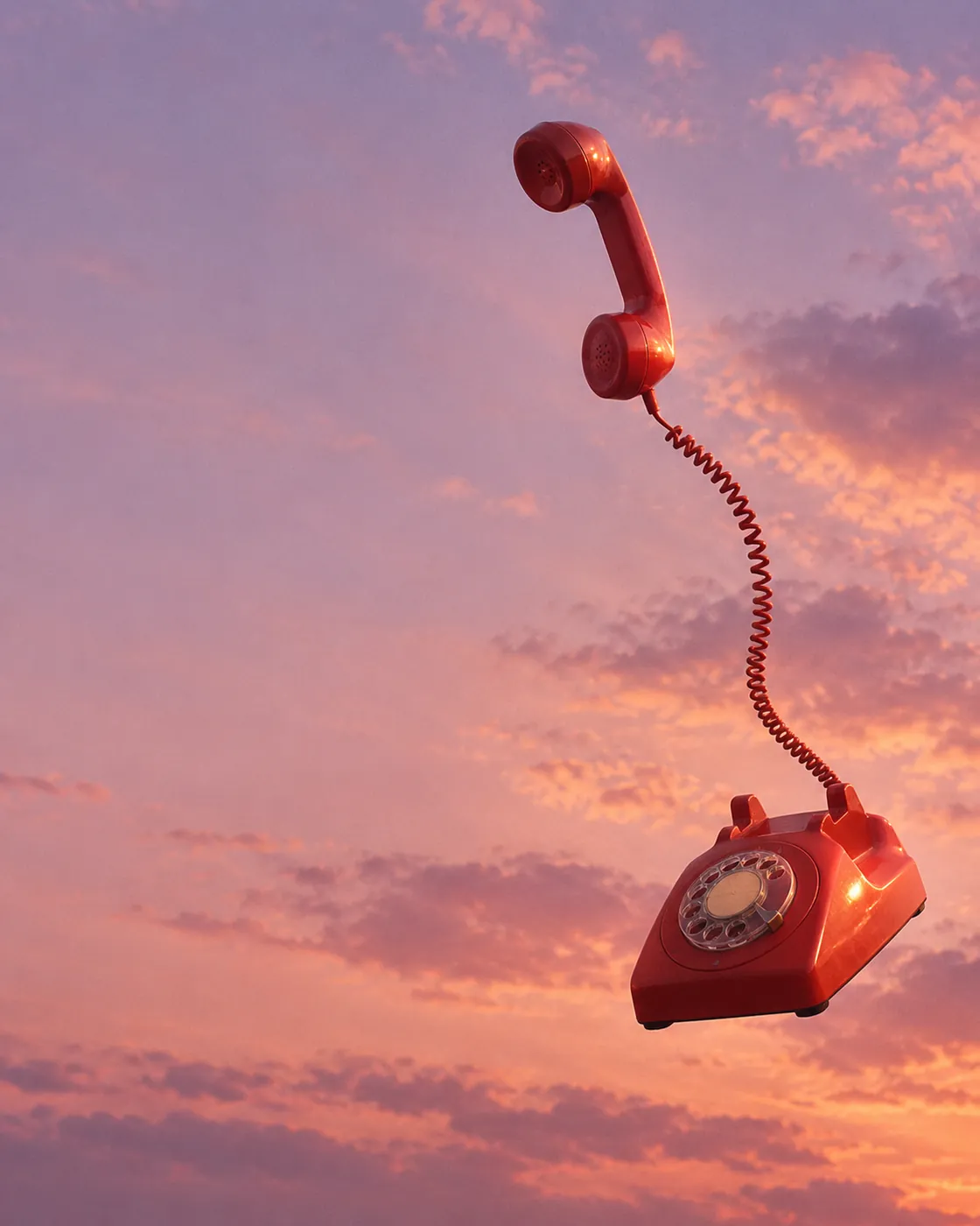 Teléfono rojo de disco volando en un cielo rosa al atardecer