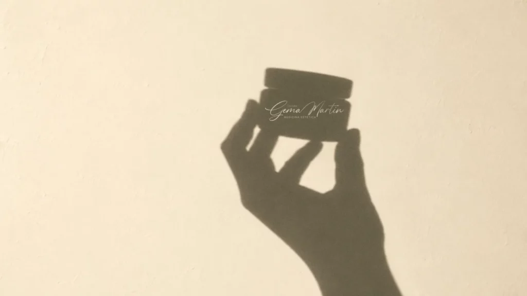 Sombra de una mano que sostiene un tarro de crema con el logotipo de la Doctora Gema Martín, Medicina Estética, sobre una pared clara